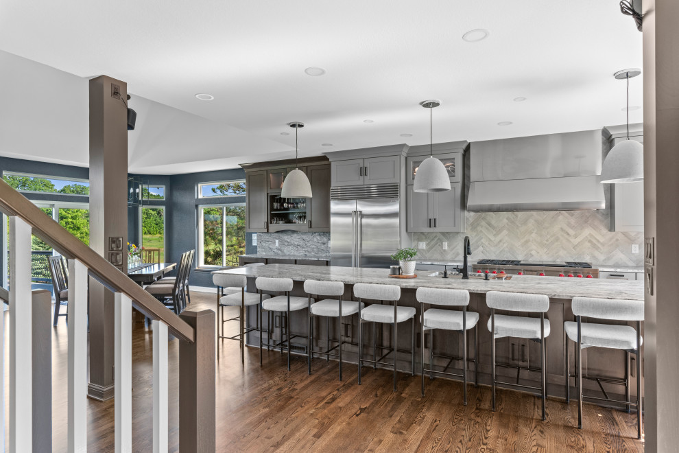 Kitchen - transitional galley dark wood floor and brown floor kitchen idea in Milwaukee with an undermount sink, shaker cabinets, gray cabinets, gray backsplash, stainless steel appliances, an island and gray countertops