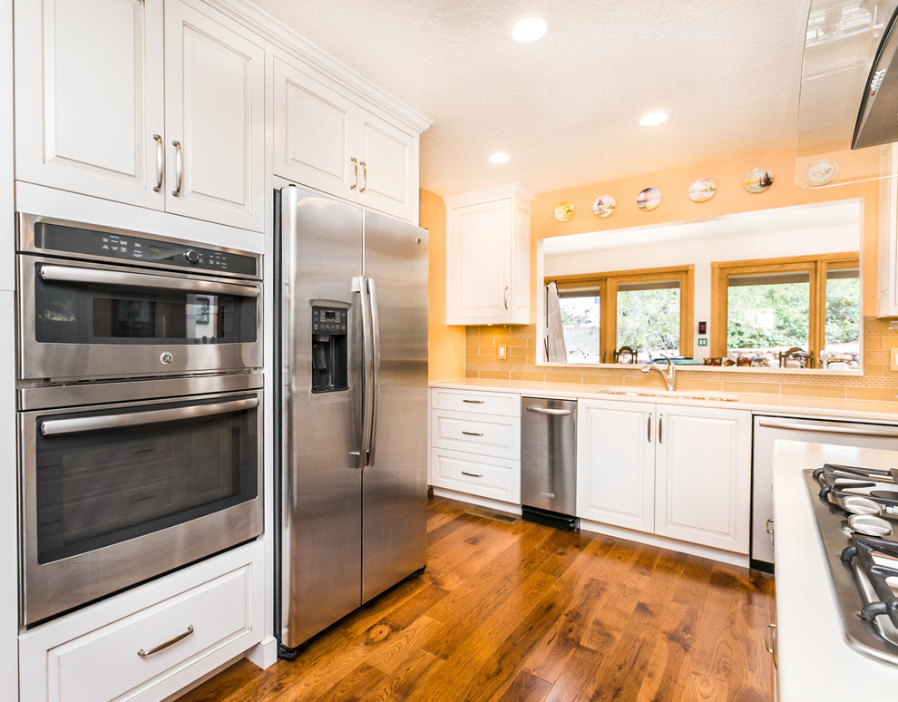 This is an example of a mid-sized transitional u-shaped separate kitchen in Albuquerque with white cabinets, quartz benchtops, beige splashback, subway tile splashback, stainless steel appliances, medium hardwood floors, with island, a double-bowl sink and raised-panel cabinets.