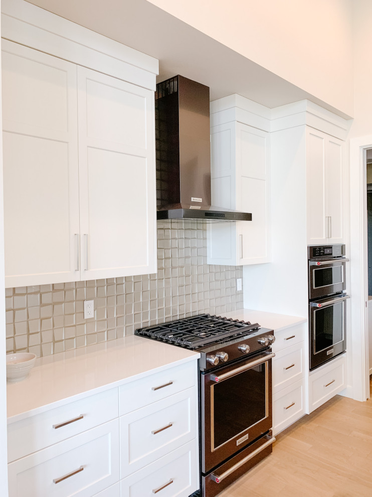 Light wood floor and beige floor eat-in kitchen photo with shaker cabinets, white cabinets, quartz countertops, gray backsplash, glass tile backsplash, black appliances and white countertops