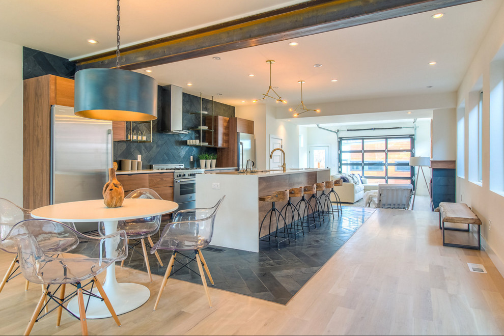 This is an example of an industrial galley open plan kitchen in Denver with flat-panel cabinets, medium wood cabinets, grey splashback, stainless steel appliances, light hardwood floors and with island.
