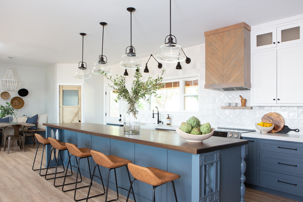 Mid-sized farmhouse porcelain tile and beige floor eat-in kitchen photo in Phoenix with a farmhouse sink, shaker cabinets, blue cabinets, quartz countertops, white backsplash, porcelain backsplash, stainless steel appliances, an island and white countertops
