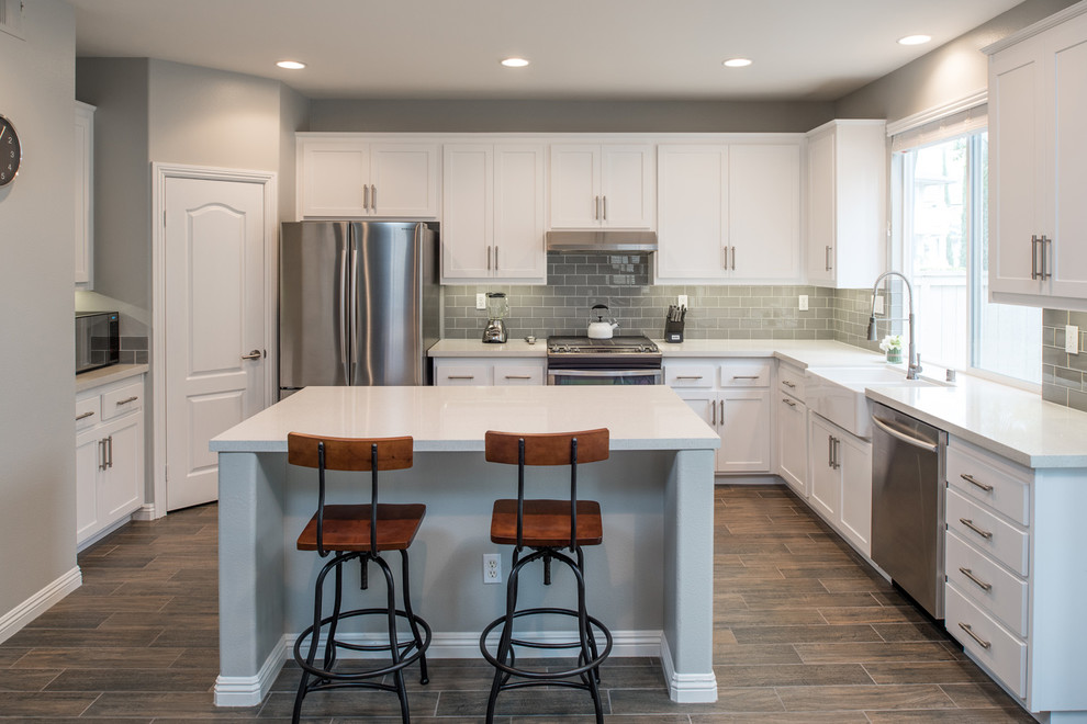 Inspiration for a mid-sized modern u-shaped kitchen in San Diego with a farmhouse sink, shaker cabinets, white cabinets, quartz benchtops, grey splashback, subway tile splashback, stainless steel appliances, plywood floors and with island.