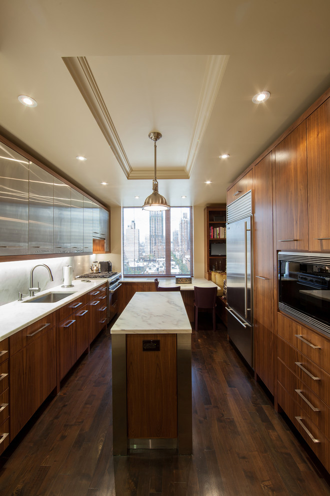 Photo of a contemporary galley kitchen in New York with an undermount sink, flat-panel cabinets, dark wood cabinets, white splashback, stainless steel appliances, dark hardwood floors and with island.