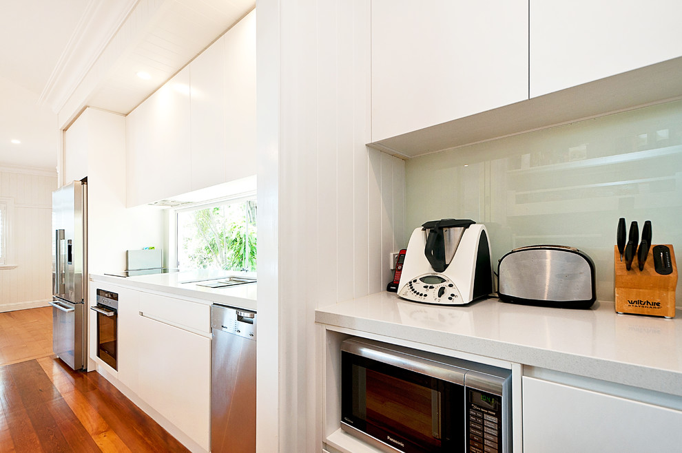 Design ideas for a large modern galley open plan kitchen in Brisbane with an undermount sink, flat-panel cabinets, white cabinets, quartz benchtops, stainless steel appliances, light hardwood floors and with island.
