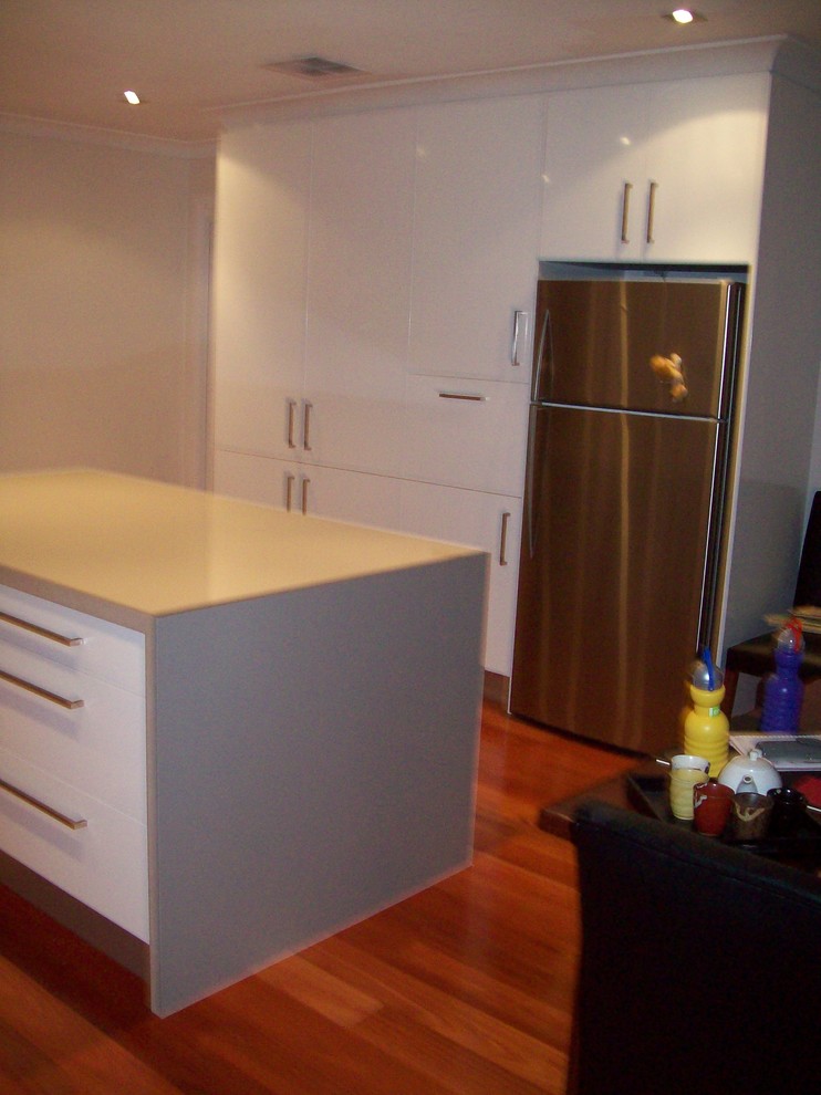 This is an example of a mid-sized modern u-shaped eat-in kitchen in Sydney with a drop-in sink, white cabinets, quartz benchtops, red splashback, glass sheet splashback, stainless steel appliances, medium hardwood floors and with island.