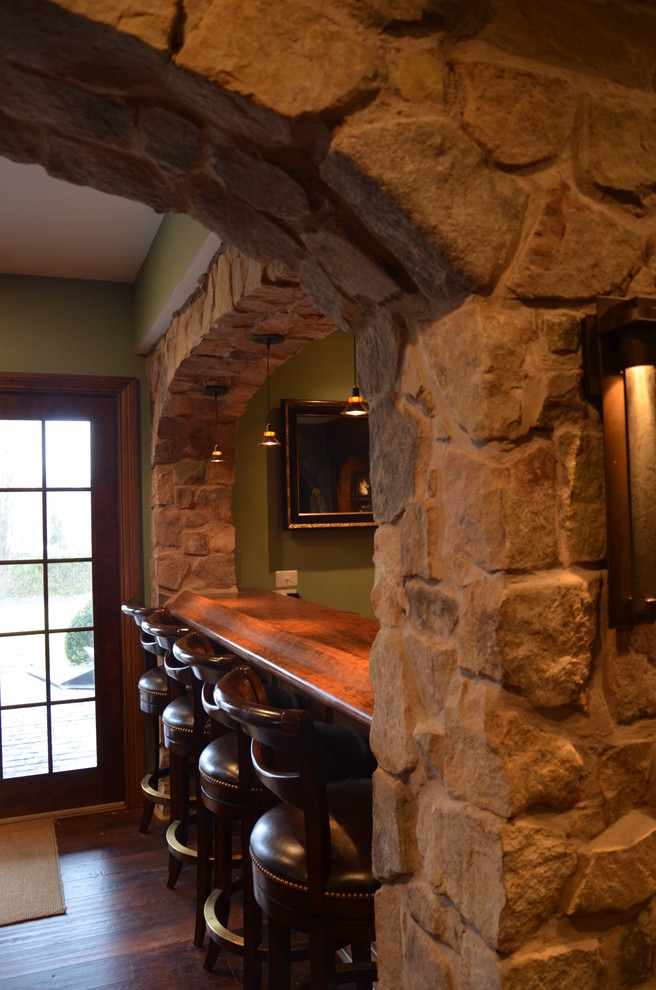 This is an example of a large traditional walk-out basement in Philadelphia with green walls, dark hardwood floors, a standard fireplace, a stone fireplace surround and brown floor.