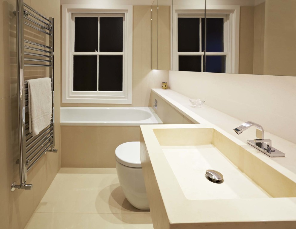 Photo of a small contemporary kids bathroom in London with an integrated sink, flat-panel cabinets, limestone benchtops, a drop-in tub, a one-piece toilet, beige tile, porcelain tile, beige walls and porcelain floors.