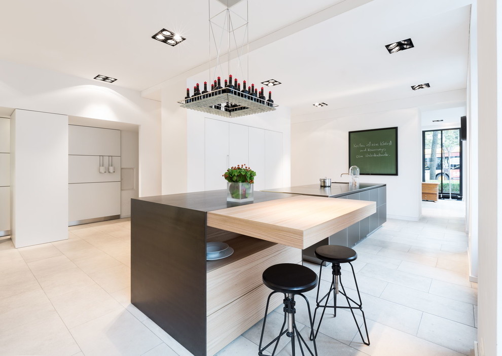 Expansive contemporary single-wall open plan kitchen in Cologne with flat-panel cabinets, white cabinets, stainless steel benchtops, multiple islands, an integrated sink and limestone floors.