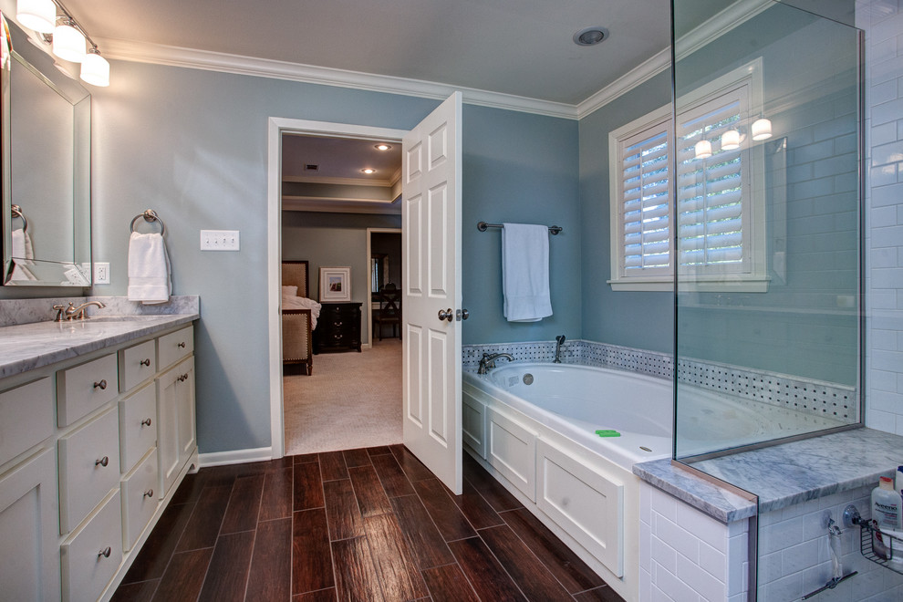 This is an example of a mid-sized traditional master bathroom in Little Rock with raised-panel cabinets, white cabinets, a corner tub, an open shower, a one-piece toilet, gray tile, white tile, blue walls, dark hardwood floors, a drop-in sink and stainless steel benchtops.