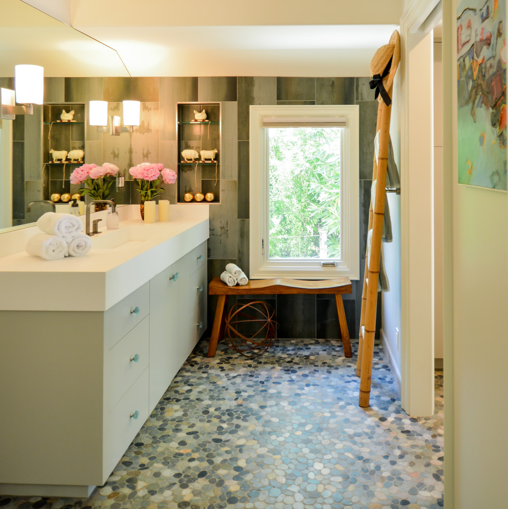 Inspiration for a mid-sized beach style 3/4 bathroom in San Francisco with flat-panel cabinets, grey cabinets, an alcove shower, a wall-mount toilet, green tile, porcelain tile, beige walls, pebble tile floors, a trough sink, solid surface benchtops, green floor and a sliding shower screen.