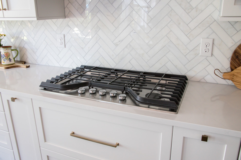Inspiration for a large transitional galley medium tone wood floor and brown floor open concept kitchen remodel in Denver with an undermount sink, shaker cabinets, white cabinets, quartz countertops, beige backsplash, marble backsplash, stainless steel appliances, an island and white countertops
