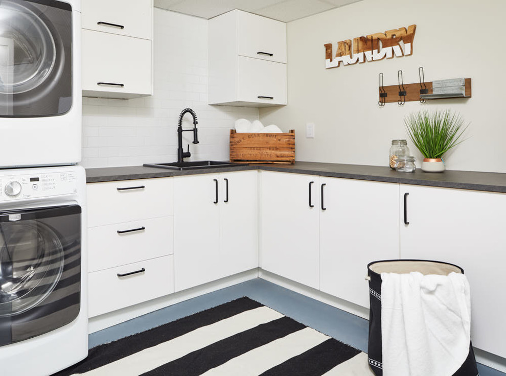 Design ideas for a country l-shaped dedicated laundry room in Toronto with a drop-in sink, flat-panel cabinets, white cabinets, grey walls, a stacked washer and dryer, blue floor and grey benchtop.