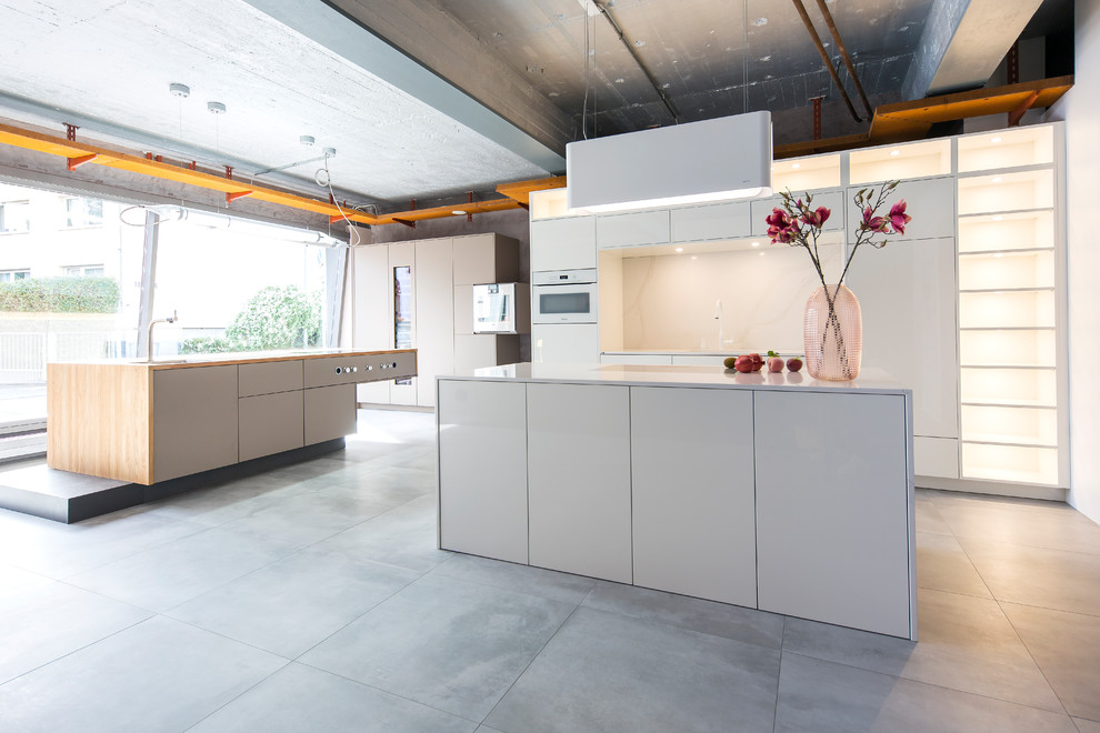 Inspiration for a mid-sized modern single-wall open plan kitchen in Frankfurt with an undermount sink, flat-panel cabinets, white cabinets, quartz benchtops, white splashback, white appliances, cement tiles, with island, grey floor and white benchtop.