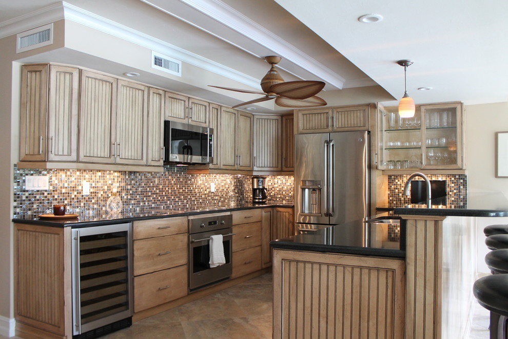 This is an example of a mid-sized tropical u-shaped eat-in kitchen in Miami with an undermount sink, medium wood cabinets, granite benchtops, multi-coloured splashback, glass tile splashback, stainless steel appliances, travertine floors, with island and louvered cabinets.