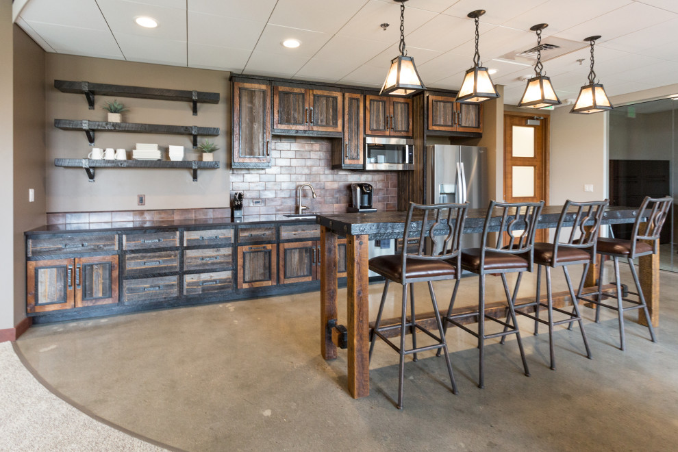 Photo of a large country single-wall eat-in kitchen in Other with an undermount sink, recessed-panel cabinets, distressed cabinets, quartzite benchtops, metallic splashback, metal splashback, stainless steel appliances, concrete floors, with island, grey floor and black benchtop.