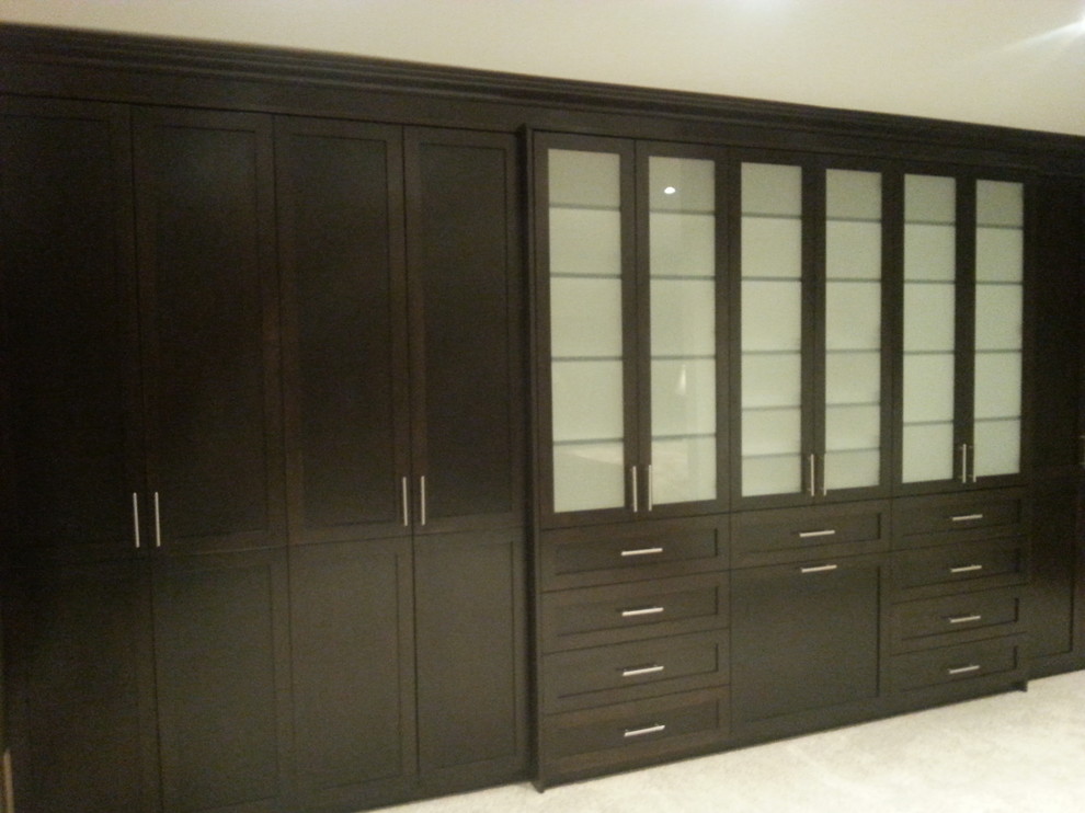Photo of a large arts and crafts gender-neutral built-in wardrobe in Vancouver with glass-front cabinets, dark wood cabinets, ceramic floors and beige floor.