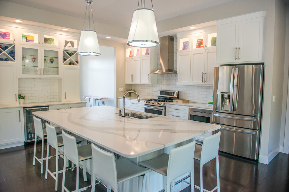 Open concept kitchen - huge transitional l-shaped dark wood floor and brown floor open concept kitchen idea with a double-bowl sink, shaker cabinets, white cabinets, quartz countertops, white backsplash, ceramic backsplash, stainless steel appliances and an island