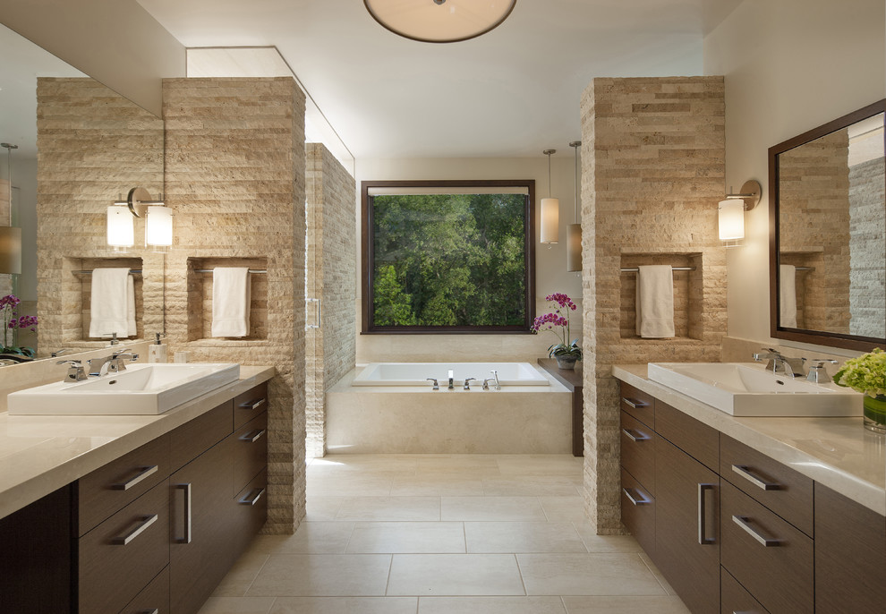 Photo of a contemporary master bathroom in Denver with a vessel sink, flat-panel cabinets, dark wood cabinets, marble benchtops, travertine floors, a drop-in tub, beige tile, beige walls and travertine.