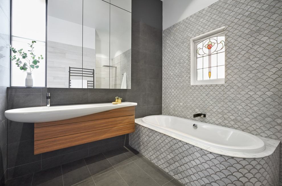 This is an example of a mid-sized contemporary master bathroom in Melbourne with glass-front cabinets, medium wood cabinets, a corner tub, an open shower, pebble tile, a vessel sink and laminate benchtops.