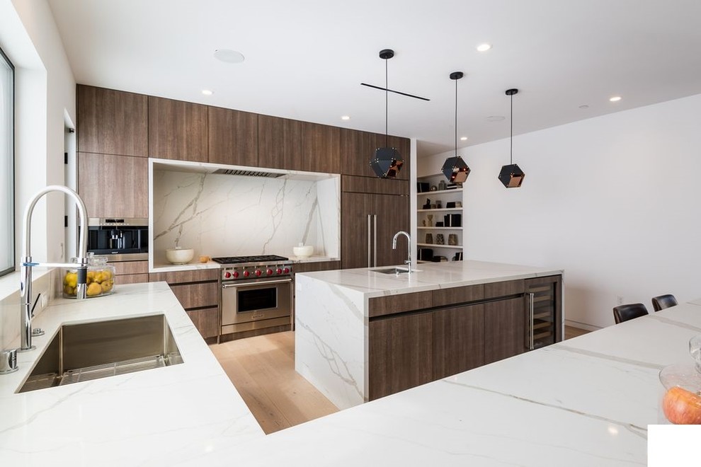 Mid-sized modern u-shaped open plan kitchen in Los Angeles with an undermount sink, flat-panel cabinets, medium wood cabinets, marble benchtops, white splashback, marble splashback, stainless steel appliances, light hardwood floors, with island, brown floor and white benchtop.