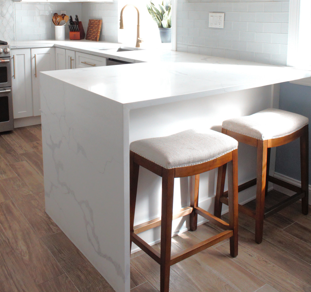 Inredning av ett modernt litet vit vitt kök, med en undermonterad diskho, skåp i shakerstil, vita skåp, bänkskiva i kvarts, blått stänkskydd, stänkskydd i porslinskakel, rostfria vitvaror, mellanmörkt trägolv, en halv köksö och brunt golv