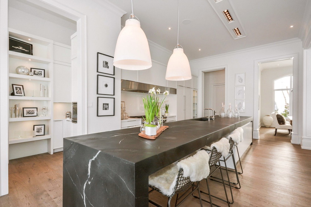 Inspiration for a transitional galley kitchen in Toronto with white cabinets, soapstone benchtops, white splashback, glass sheet splashback, panelled appliances, medium hardwood floors and with island.