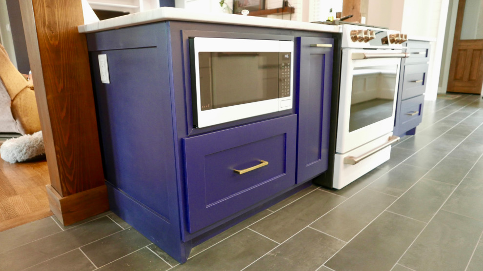 Example of a mid-sized transitional galley porcelain tile and black floor eat-in kitchen design with a farmhouse sink, shaker cabinets, blue cabinets, marble countertops, white backsplash, subway tile backsplash, white appliances, an island and multicolored countertops