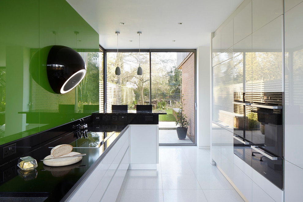 Design ideas for a contemporary kitchen in London with an integrated sink, flat-panel cabinets, white cabinets, granite benchtops, green splashback, glass sheet splashback, black appliances, porcelain floors and with island.
