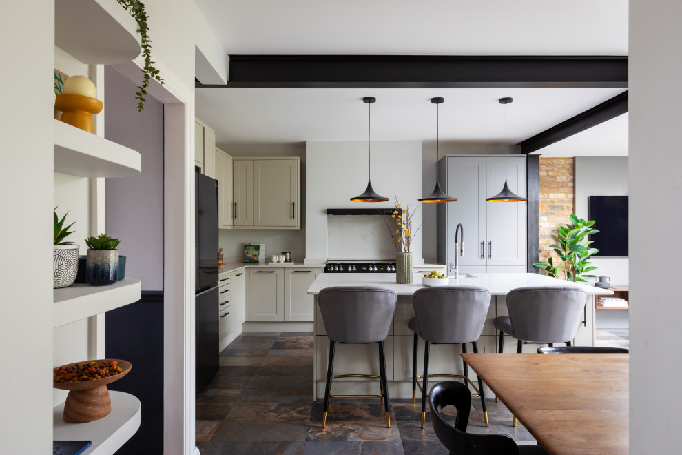 Contemporary l-shaped kitchen in London with a belfast sink, shaker cabinets, beige cabinets, black appliances, an island, multi-coloured floors and white worktops.