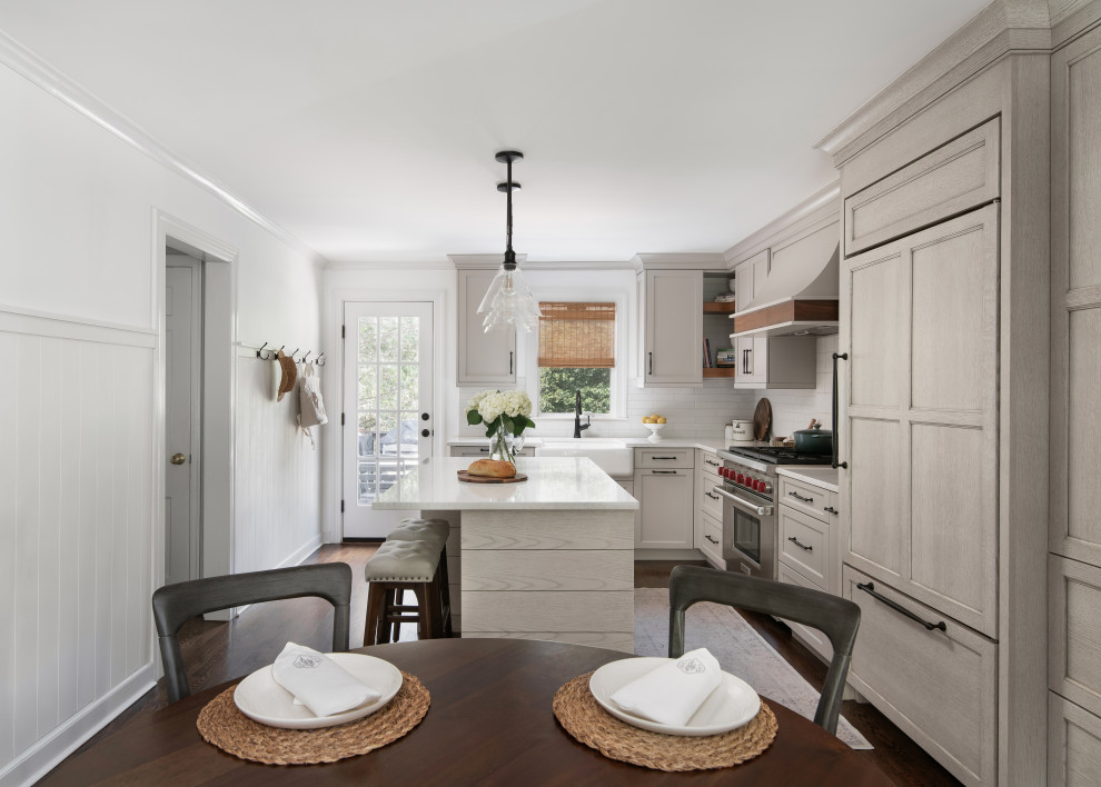 Inspiration for a mid-sized transitional l-shaped medium tone wood floor and brown floor eat-in kitchen remodel in New York with a farmhouse sink, shaker cabinets, beige cabinets, quartz countertops, white backsplash, porcelain backsplash, paneled appliances, an island and white countertops