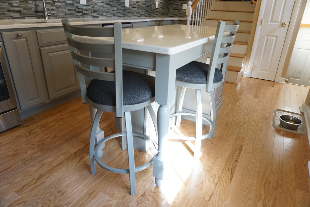 Eat-in kitchen - small traditional l-shaped medium tone wood floor eat-in kitchen idea in Providence with a triple-bowl sink, raised-panel cabinets, gray cabinets, quartz countertops, gray backsplash, mosaic tile backsplash, stainless steel appliances, an island and white countertops
