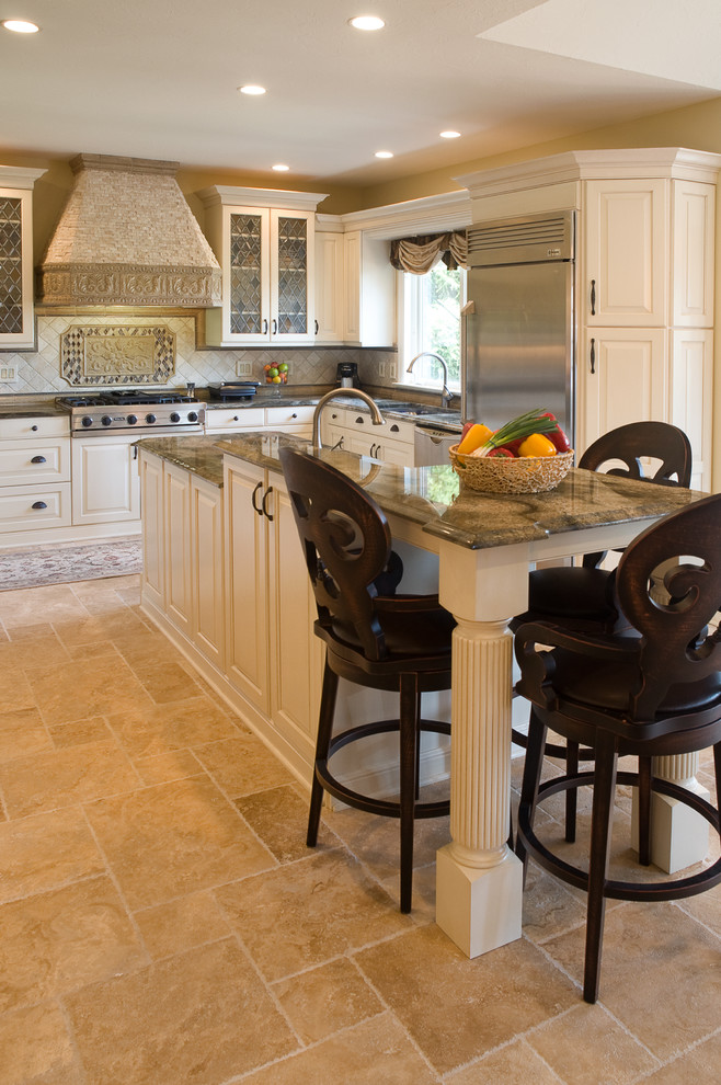 This is an example of a traditional u-shaped eat-in kitchen in Other with raised-panel cabinets, beige cabinets, granite benchtops, beige splashback, stone tile splashback, travertine floors and with island.