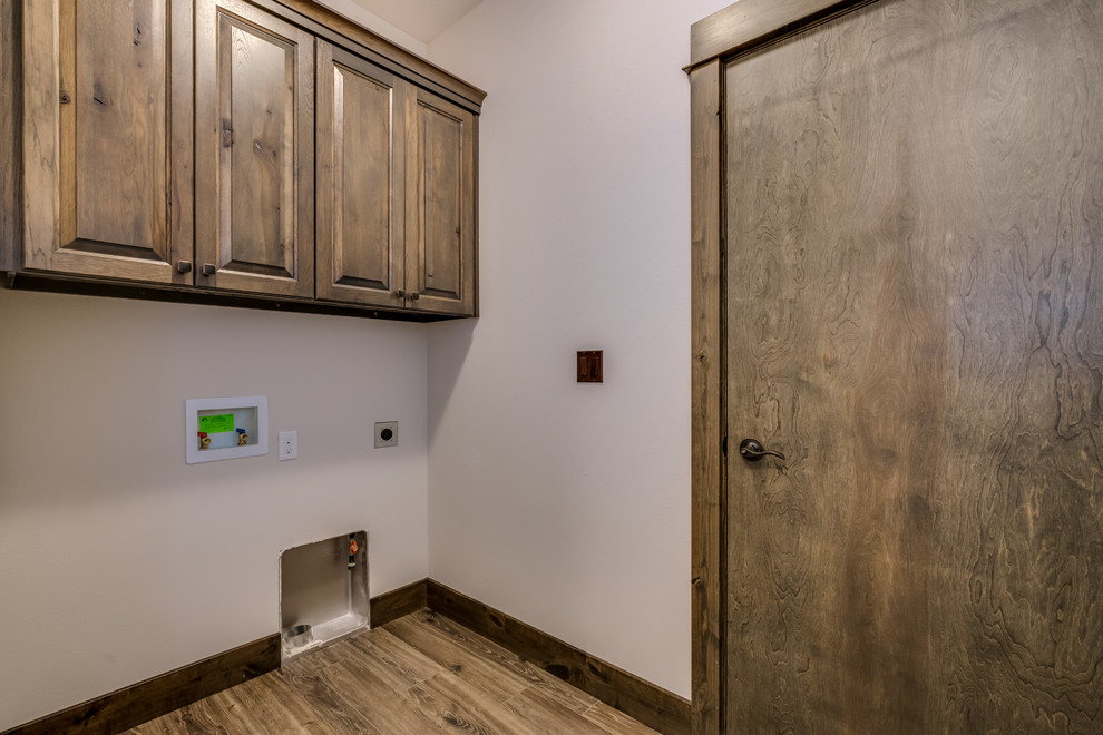 Example of a mountain style single-wall laminate floor and brown floor utility room design with raised-panel cabinets, brown cabinets, beige walls and a side-by-side washer/dryer