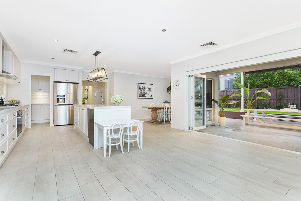 Inspiration for a mid-sized modern l-shaped open plan kitchen in Sydney with an undermount sink, shaker cabinets, white cabinets, quartz benchtops, white splashback, subway tile splashback, stainless steel appliances, terra-cotta floors, with island, beige floor and white benchtop.