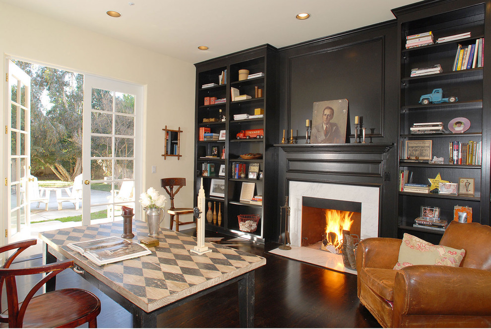 This is an example of a traditional home office in Los Angeles with white walls, dark hardwood floors, a freestanding desk and a standard fireplace.