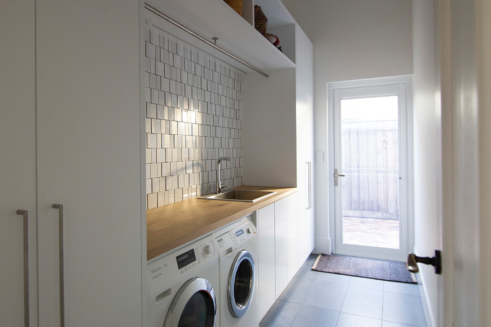 Contemporary single-wall dedicated laundry room in Perth with a drop-in sink, flat-panel cabinets, white cabinets, wood benchtops, white walls, slate floors, a side-by-side washer and dryer, grey floor and brown benchtop.