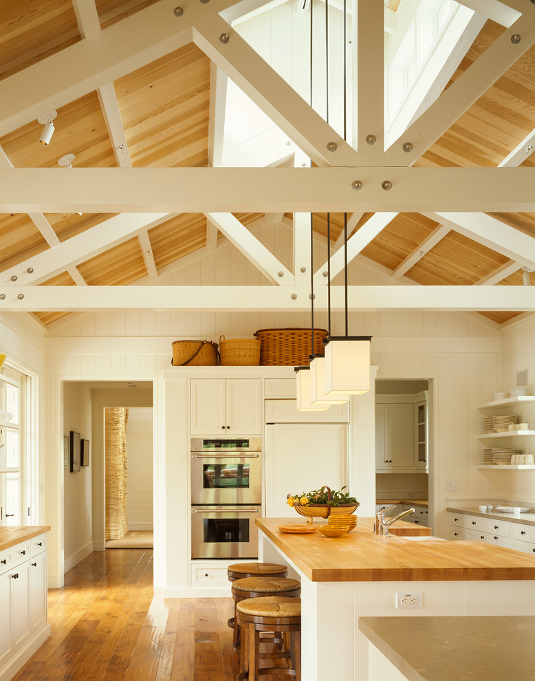 Photo of a country u-shaped kitchen in San Francisco with shaker cabinets, white cabinets, wood benchtops, medium hardwood floors, with island and stainless steel appliances.