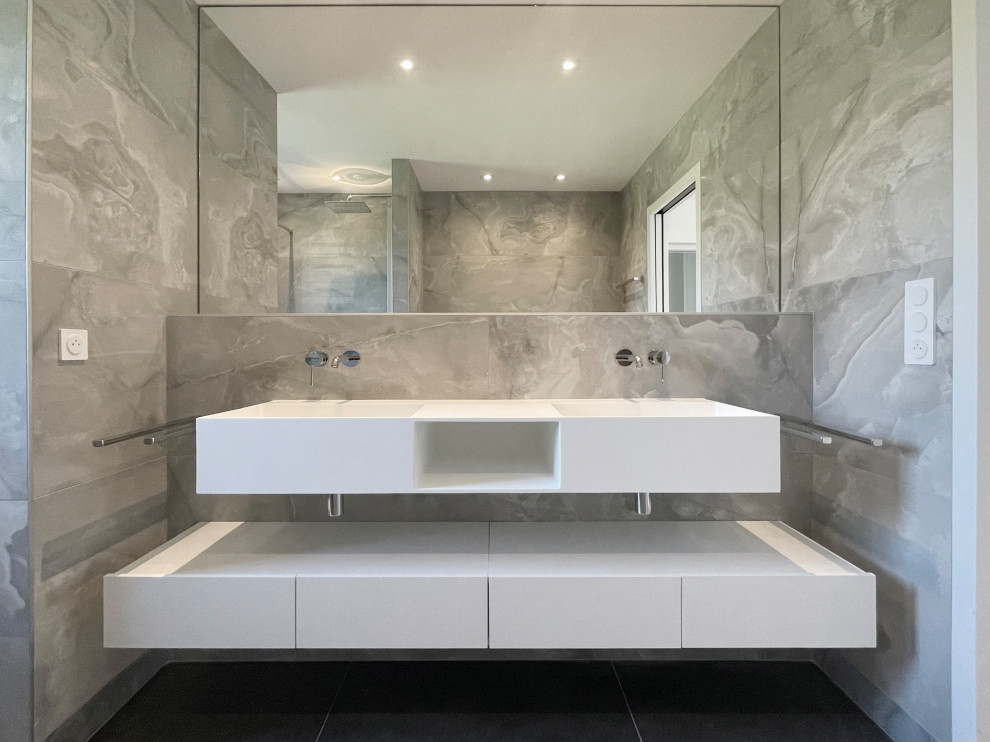 Inredning av ett modernt mellanstort vit vitt badrum med dusch, med vita skåp, en vägghängd toalettstol, grå kakel, stenkakel, grå väggar, skiffergolv, ett avlångt handfat, bänkskiva i akrylsten och grått golv
