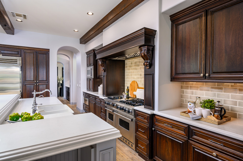 Example of a large transitional galley light wood floor and exposed beam open concept kitchen design in Phoenix with a double-bowl sink, dark wood cabinets, wood countertops, gray backsplash, ceramic backsplash, stainless steel appliances, an island and white countertops