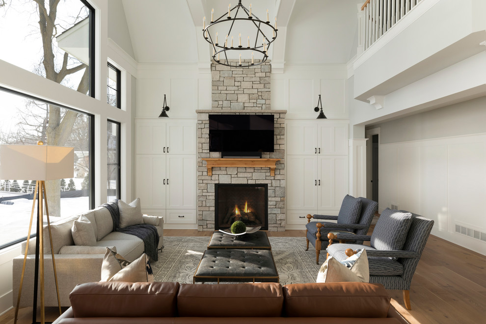 This is an example of a large transitional formal open concept living room in Minneapolis with grey walls, medium hardwood floors, a standard fireplace, a stone fireplace surround, a wall-mounted tv and brown floor.