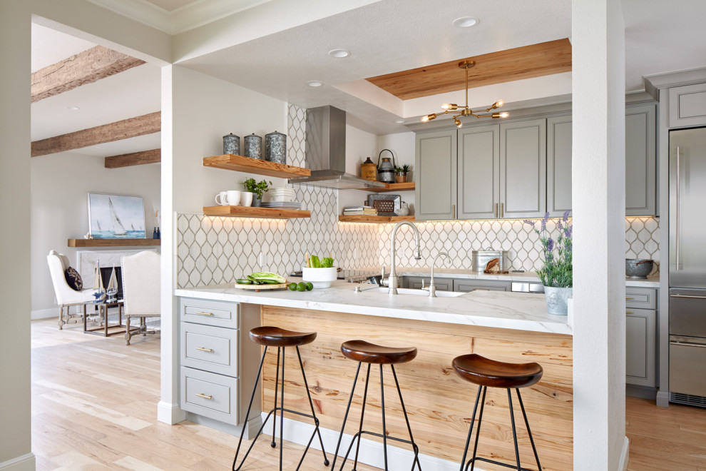 Inspiration for a large beach style u-shaped eat-in kitchen in San Francisco with recessed-panel cabinets, grey cabinets, white splashback, stainless steel appliances, light hardwood floors, a peninsula, beige floor, white benchtop, a farmhouse sink, marble benchtops and ceramic splashback.