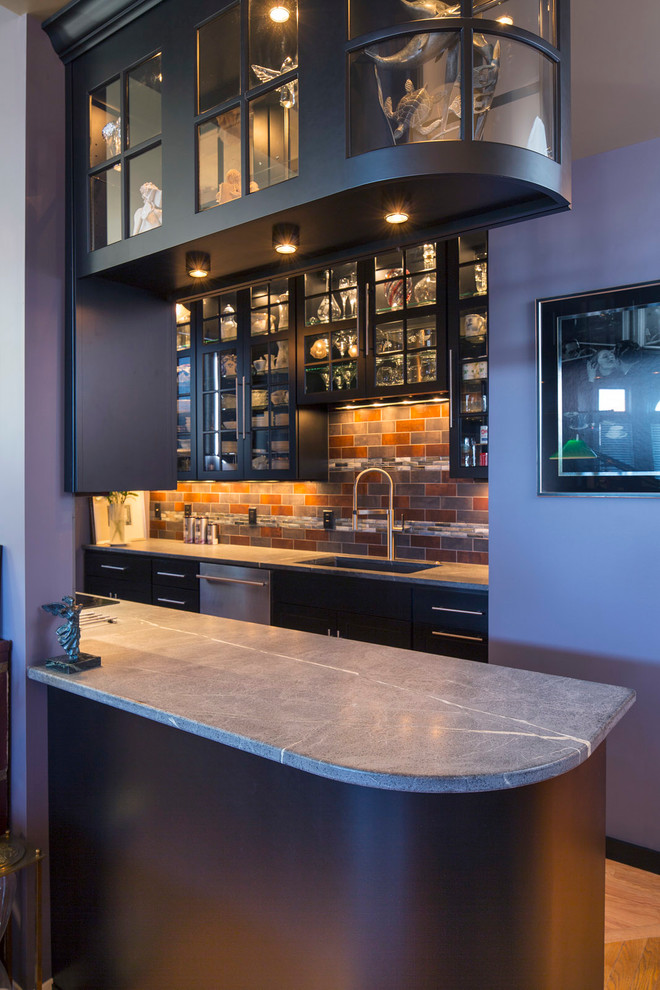 Inspiration for a small transitional galley medium tone wood floor enclosed kitchen remodel in Minneapolis with an undermount sink, glass-front cabinets, black cabinets, soapstone countertops, stainless steel appliances, a peninsula and porcelain backsplash