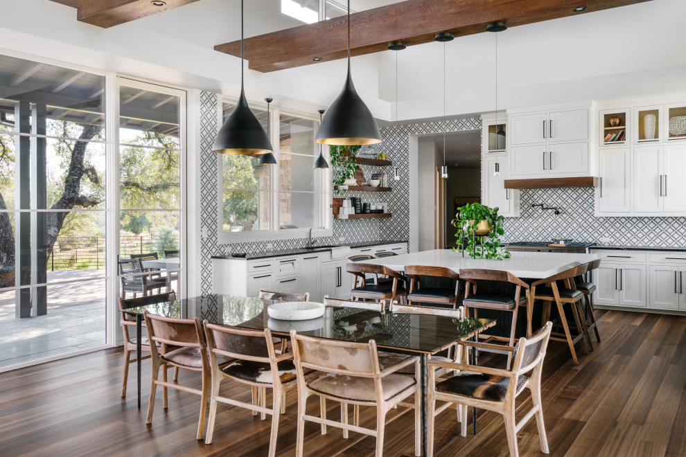 Photo of a country eat-in kitchen in Austin with an undermount sink, shaker cabinets, white cabinets, multi-coloured splashback, dark hardwood floors, with island, brown floor and black benchtop.