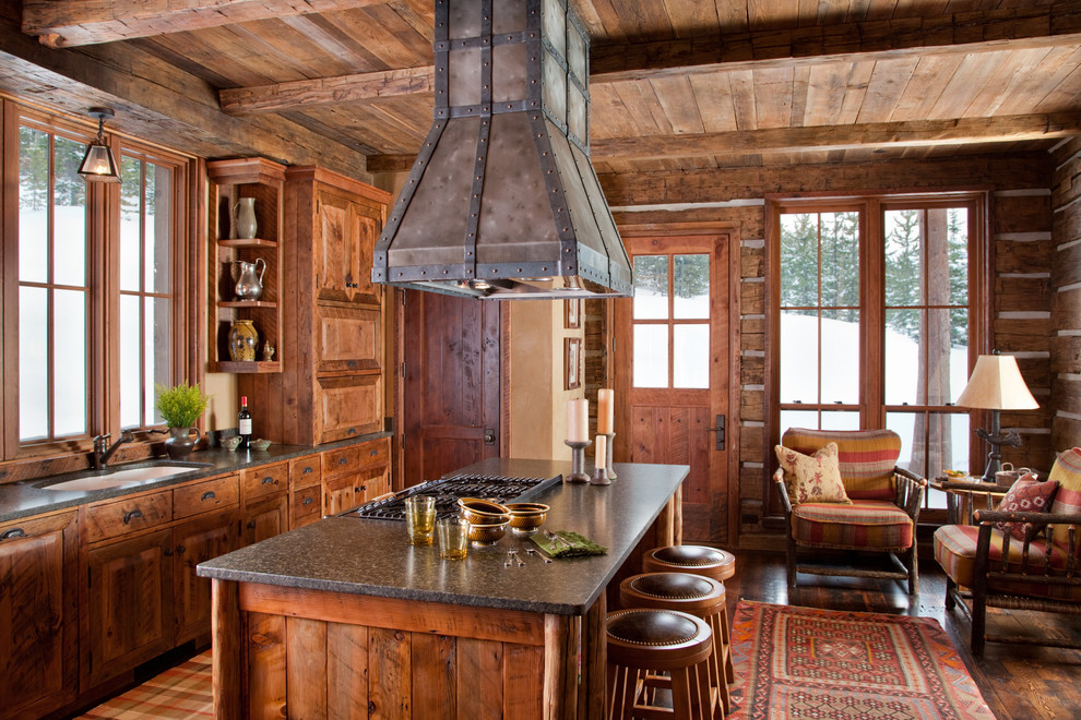 Example of a mountain style galley dark wood floor kitchen design with a double-bowl sink, raised-panel cabinets, dark wood cabinets and an island