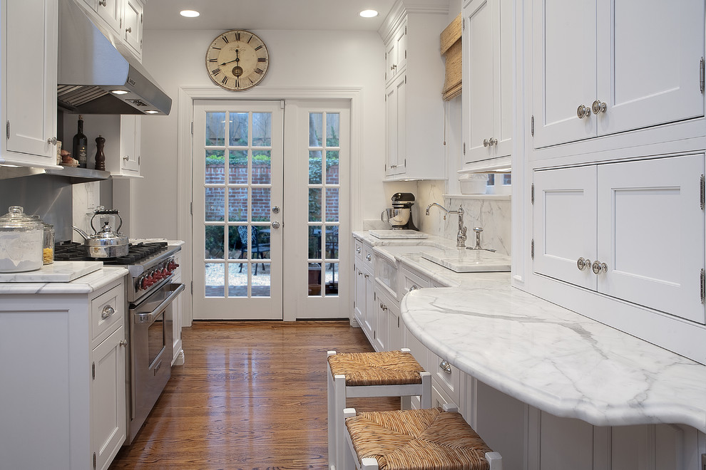 This is an example of a traditional galley separate kitchen in DC Metro with a farmhouse sink, beaded inset cabinets, white cabinets, stainless steel appliances, stone slab splashback, white splashback, marble benchtops, light hardwood floors and no island.