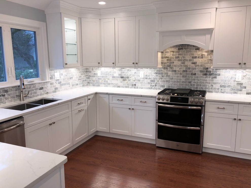Example of a mid-sized transitional u-shaped dark wood floor and brown floor enclosed kitchen design with an undermount sink, shaker cabinets, white cabinets, marble countertops, gray backsplash, stone tile backsplash, stainless steel appliances, no island and white countertops