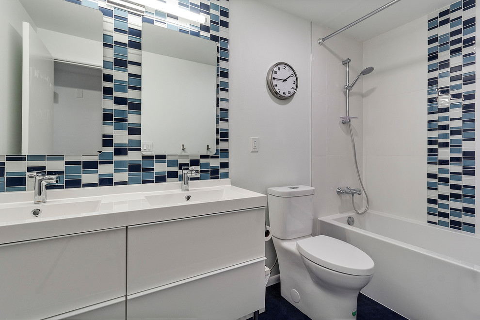 This is an example of a small modern kids bathroom in Portland with flat-panel cabinets, white cabinets, a shower/bathtub combo, blue tile, mosaic tile, white walls, linoleum floors, an integrated sink, blue floor, a shower curtain, white benchtops, a two-piece toilet and engineered quartz benchtops.