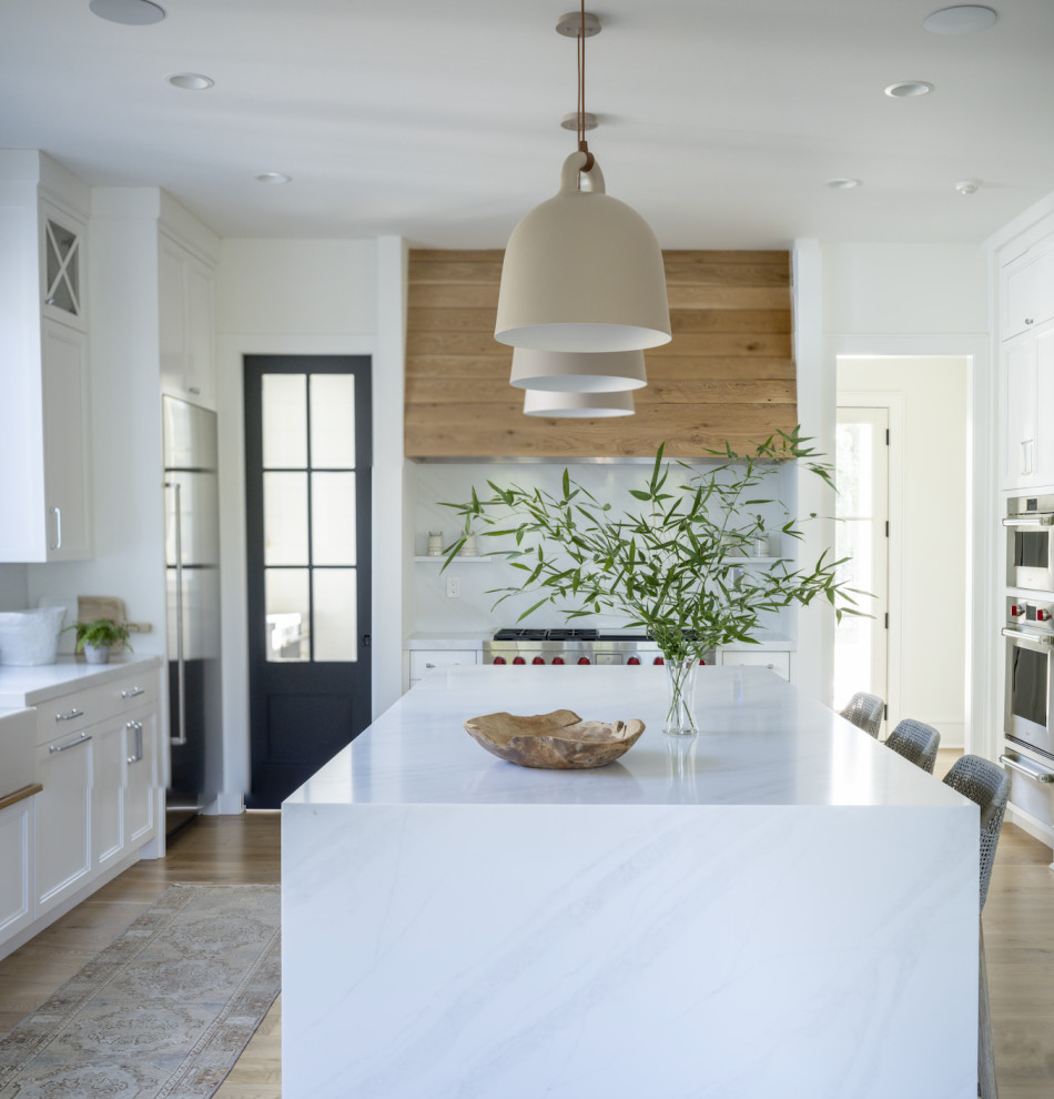 Inspiration for an expansive modern l-shaped open plan kitchen in Other with a farmhouse sink, shaker cabinets, white cabinets, quartz benchtops, white splashback, marble splashback, stainless steel appliances, light hardwood floors, with island, brown floor and white benchtop.