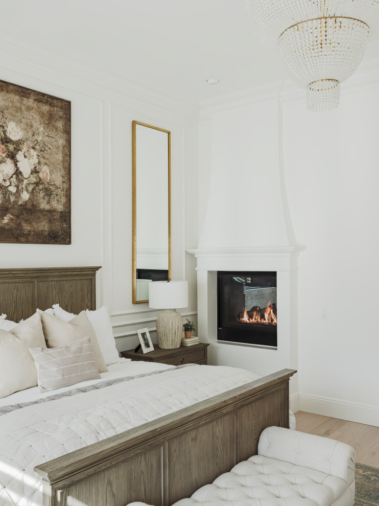 Imagen de dormitorio principal clásico renovado grande con paredes blancas, suelo de madera clara, chimenea de esquina, marco de chimenea de yeso, suelo gris, machihembrado y panelado