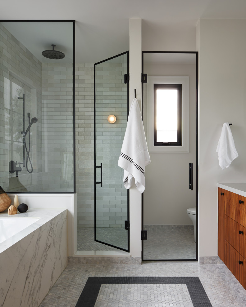 Contemporary bathroom in Toronto with flat-panel cabinets, medium wood cabinets, a submerged bath, an alcove shower, white tiles, metro tiles, white walls, mosaic tile flooring, multi-coloured floors, a hinged door, white worktops, an enclosed toilet and a built in vanity unit.